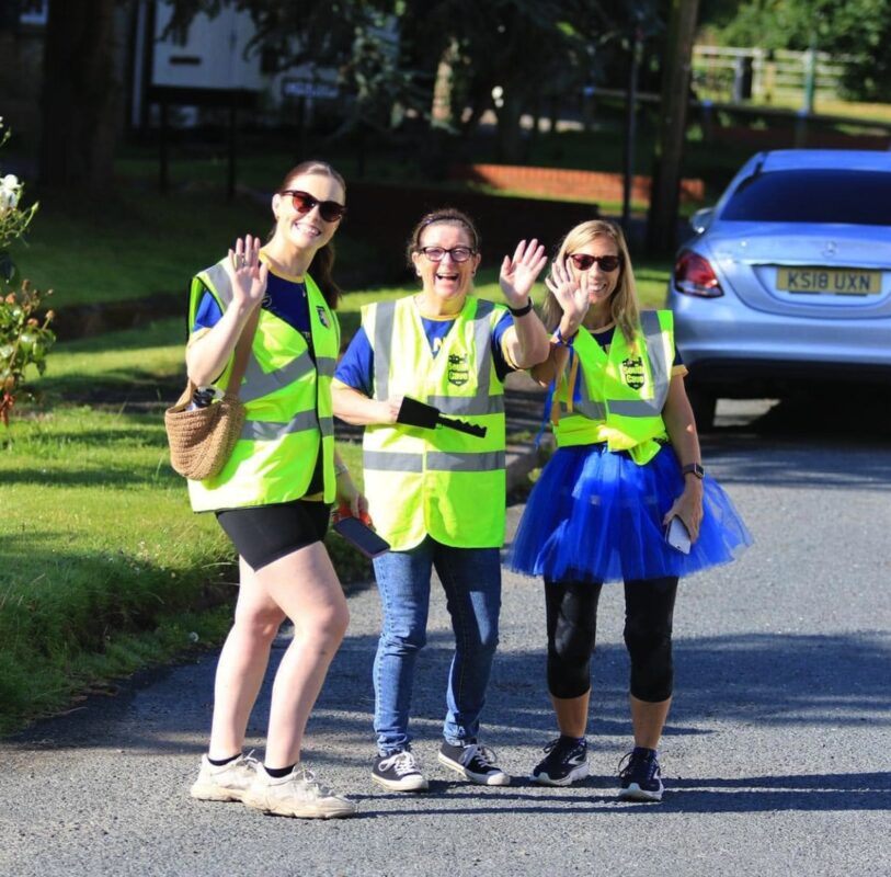 Three South Cave 10k marshals in high-vis vests waving from the roadside